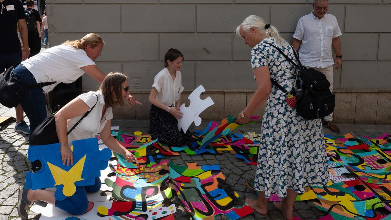 image:Image Účastníci česko-německého setkání společně skládají obří puzzle na plzeňském náměstí. Barevný střed vytvořily děti a mladí lidé, motto „Bez hranic spojeni“ symbolizuje propojení Evropy.