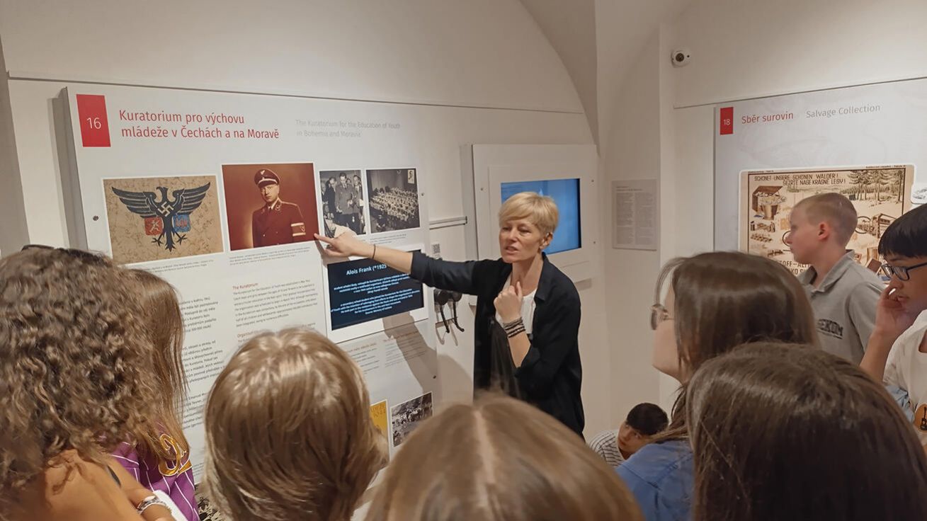 image:Image Lektorka Dana Terragni vysvětluje studentům, co bylo Kuratorium pro výchovu mládeže v Čechách a na Moravě, kde by je během války vychovávali
v nacistickém duchu.
